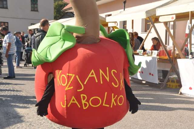 Na fotografiji je človek oblečen v kostum kozjanskega jabolka. V ozadju je trg s stojnicami in množico ljudi.